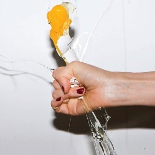 Hand squeezing a glass of broken egg with yolk running down.