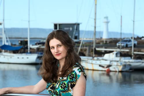 Woman with wavy brown hair at a marina with sailboats.