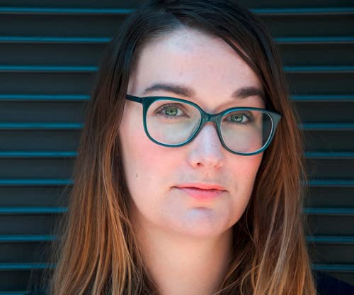 Close-up of a woman with brown hair and teal-framed glasses.