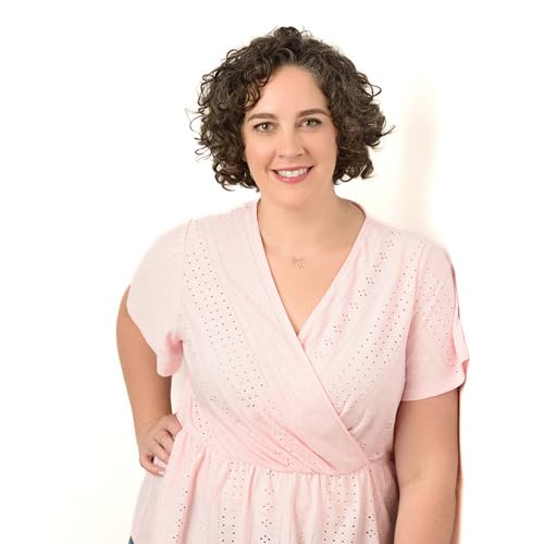 Woman with curly hair smiling, wearing a light pink wrap top.