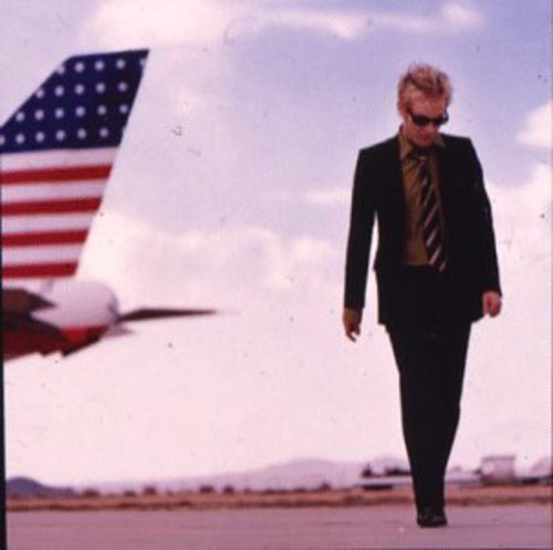 CD cover: man in suit walking near a blurred airplane tail.