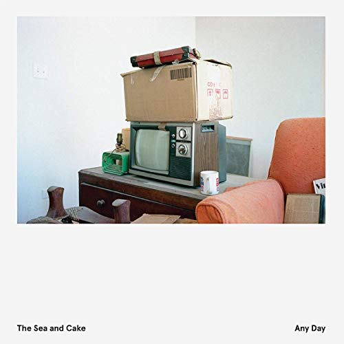 CD cover with stacked boxes, a vintage TV, and orange chair.