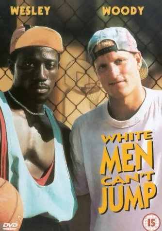 Two men in casual clothes and caps stand in front of a chain link fence.