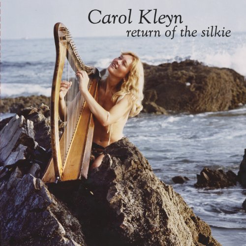 Woman playing a harp on rocks by the ocean.