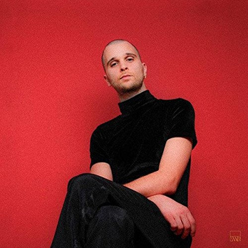 Portrait of a bald man in black clothing against a red background.