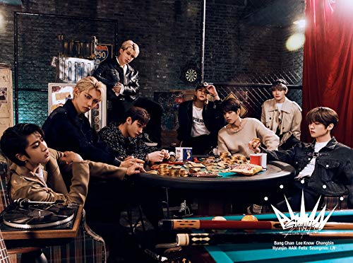 Stray Kids, eight members posed around a table in a dimly lit room.
