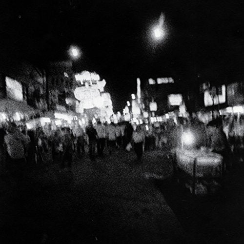 Black and white, blurry image of a crowded, illuminated street scene.