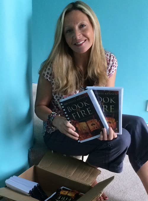 A blonde woman holding two copies of the book Book of Fire.