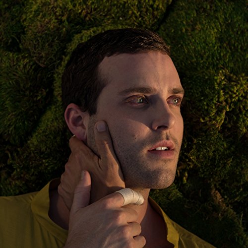 Close-up of a man with a bandaged hand touching his face, moss background.