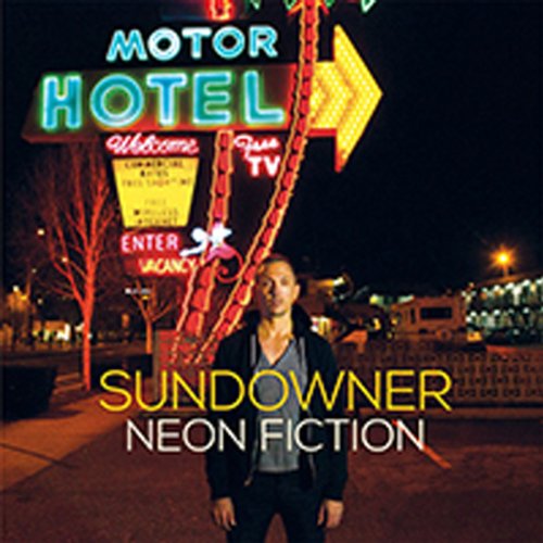 Man stands before a brightly lit, vintage motor hotel at night.