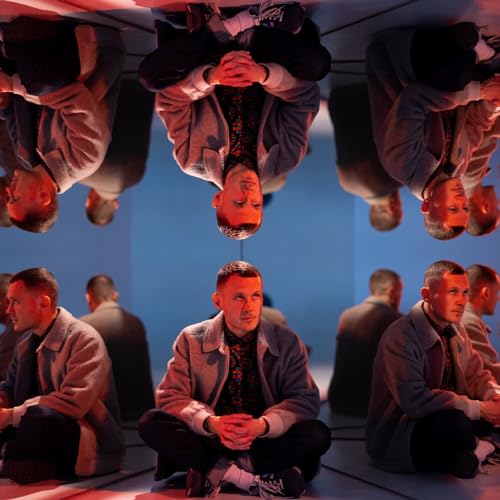 Man in light jacket seated, reflected in mirrored room.