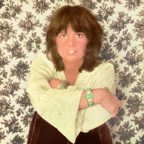 Linda Ronstadt portrait, wearing a white blouse and bracelets, floral background.