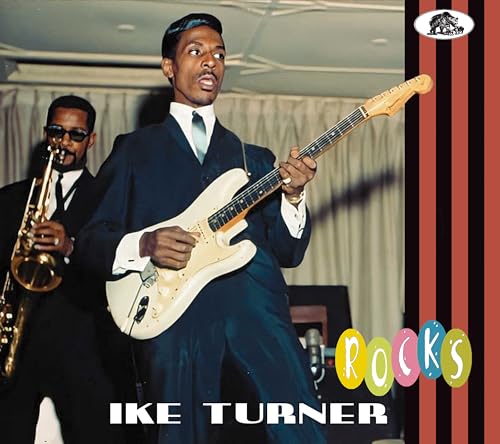 Ike Turner playing a white electric guitar with a saxophonist behind him.