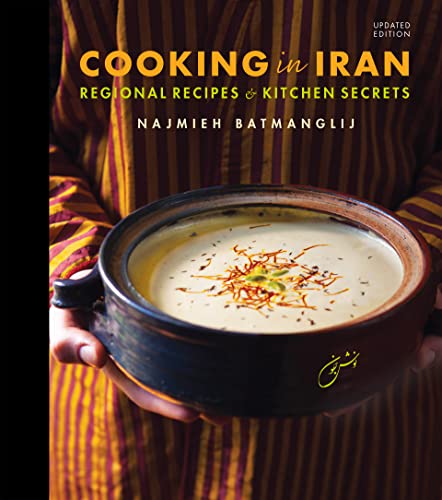 A person holds a bowl of creamy soup garnished with herbs and spices.
