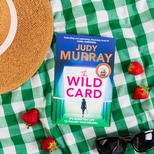 The Wild Card book cover on a green checkered picnic blanket with strawberries and sunglasses.