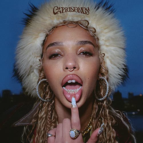 Fka Twigs portrait with a fluffy hat, open mouth, and raised finger.