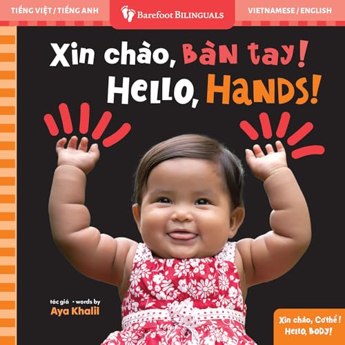 A baby in a floral dress raises both hands against a black background.
