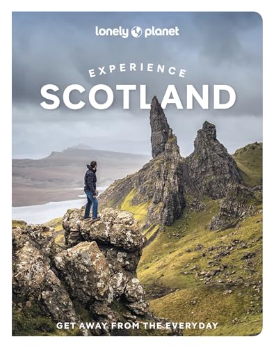 A person stands on a rocky cliff overlooking a mountainous landscape in Scotland.