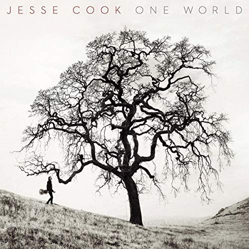 Black and white image of a man walking with a guitar under a bare tree.
