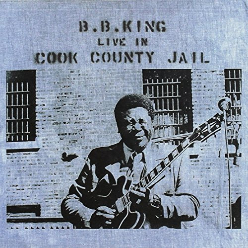 B.B. King playing guitar in front of a brick wall with jail bars.