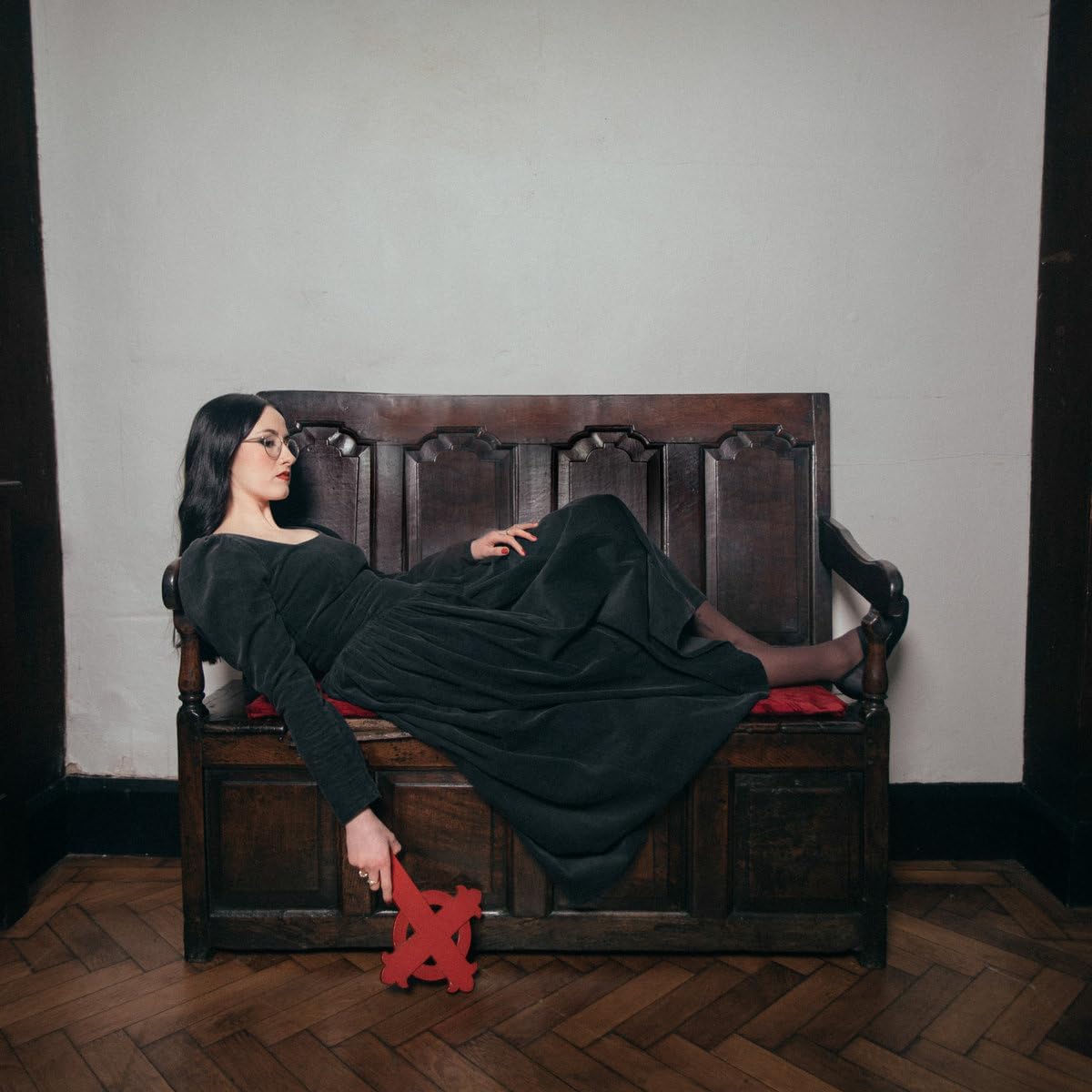 Woman in black dress reclines on a wooden bench, holding a red object.
