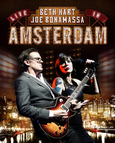 Joe Bonamassa playing guitar next to singer Beth Hart against an Amsterdam cityscape background.