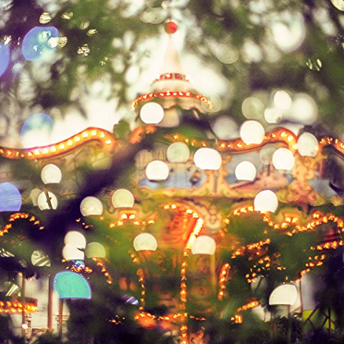 Blurred image of a carousel with bright lights, seen through foliage.