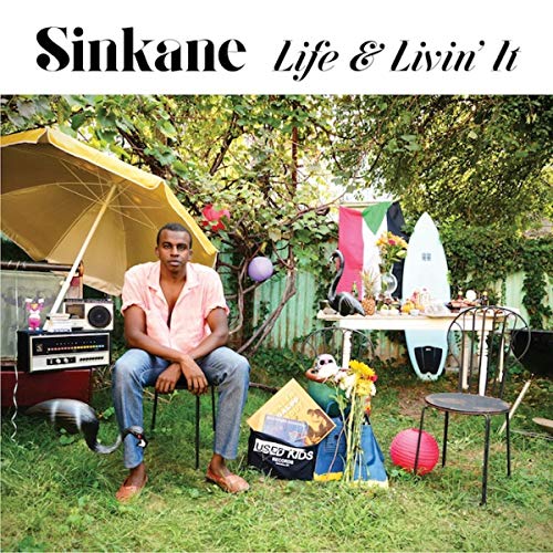 Sinkane album cover: man seated in a backyard with colorful objects.