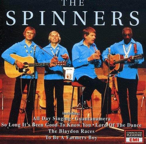 Four men in blue shirts performing on stage with acoustic guitars and microphones.