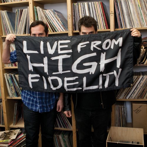 Two men hold a black banner reading "Live From High Fidelity" in front of records.