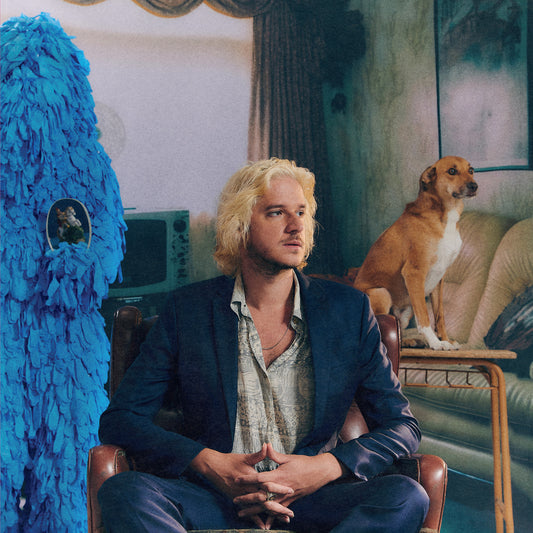 Blond man in suit sits with dog and blue sculpture.