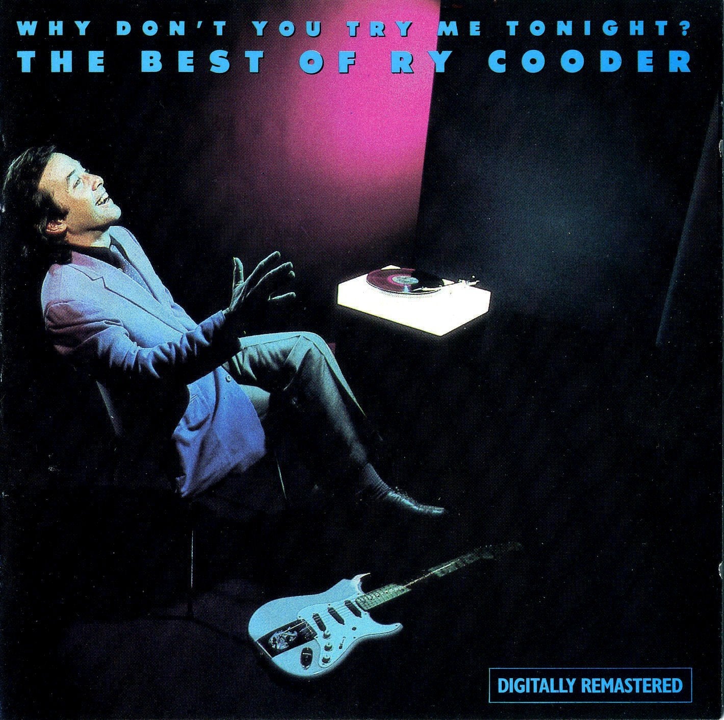 Ry Cooder sits in a chair with a record player and electric guitar nearby.