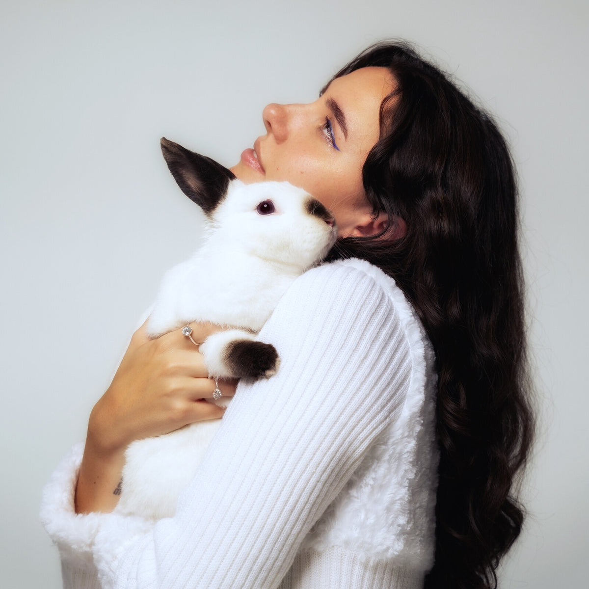 Woman with long dark hair holding a white rabbit close.