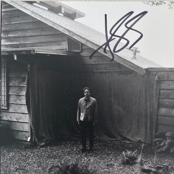 Black and white album cover featuring a man standing before a wooden building.
