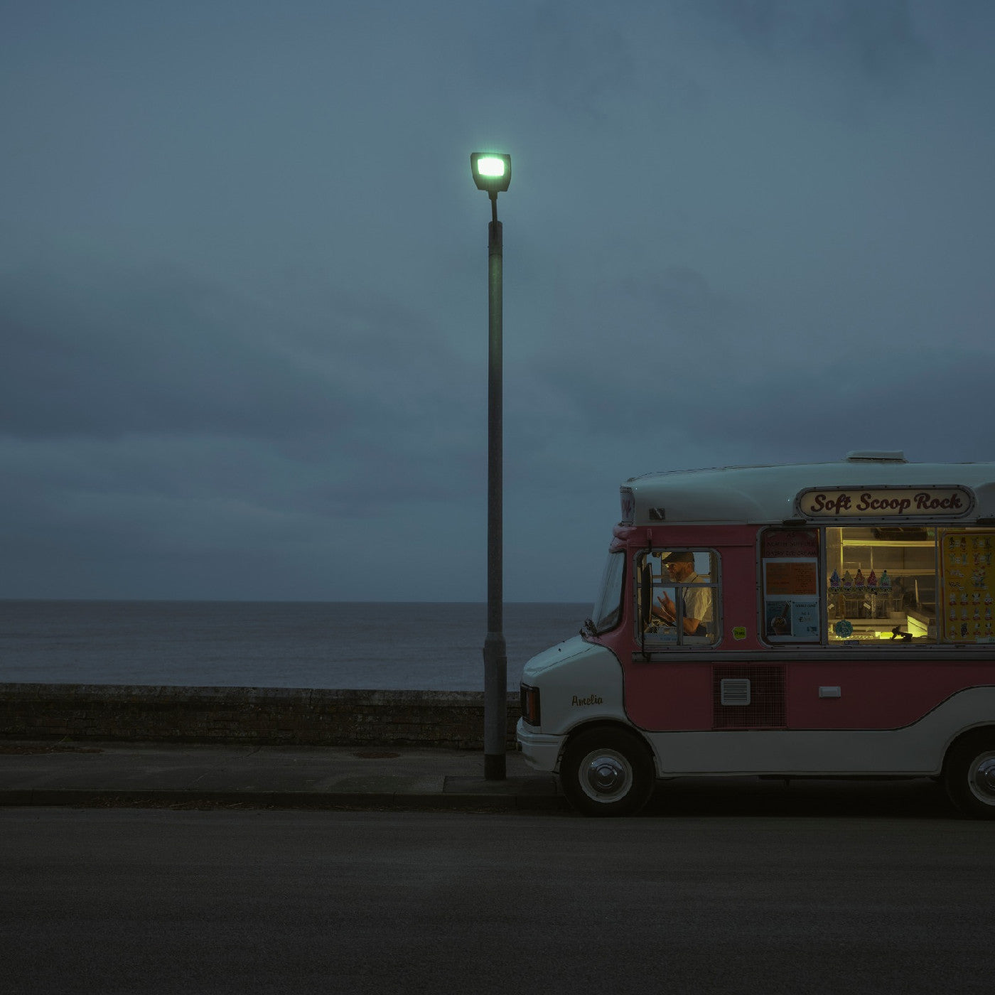 Ice cream truck parked beside a sea wall under a cloudy sky.