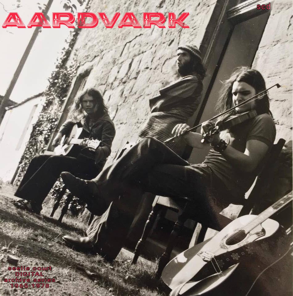 Black and white photo of three musicians playing instruments against a stone wall.