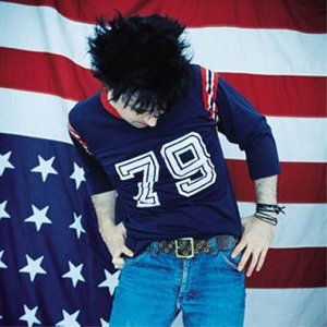 Man with dark hair wearing a football jersey in front of a flag.