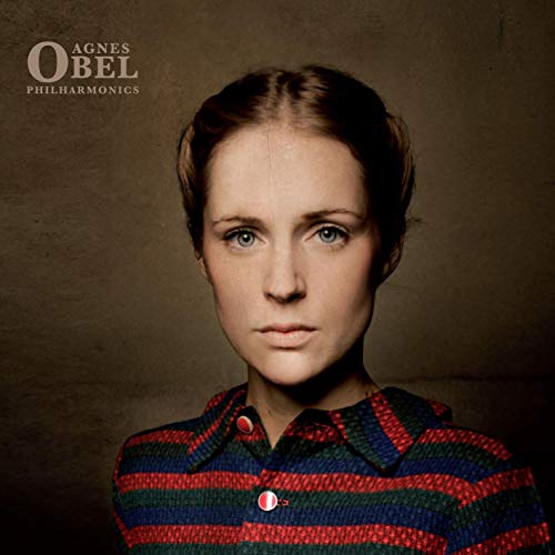 Portrait of Agnes Obel wearing a striped shirt against a dark, textured background.
