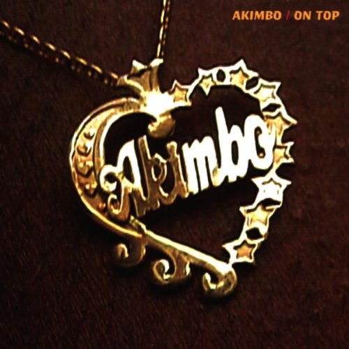 Gold heart-shaped pendant with "Akimbo" text, against a dark background.