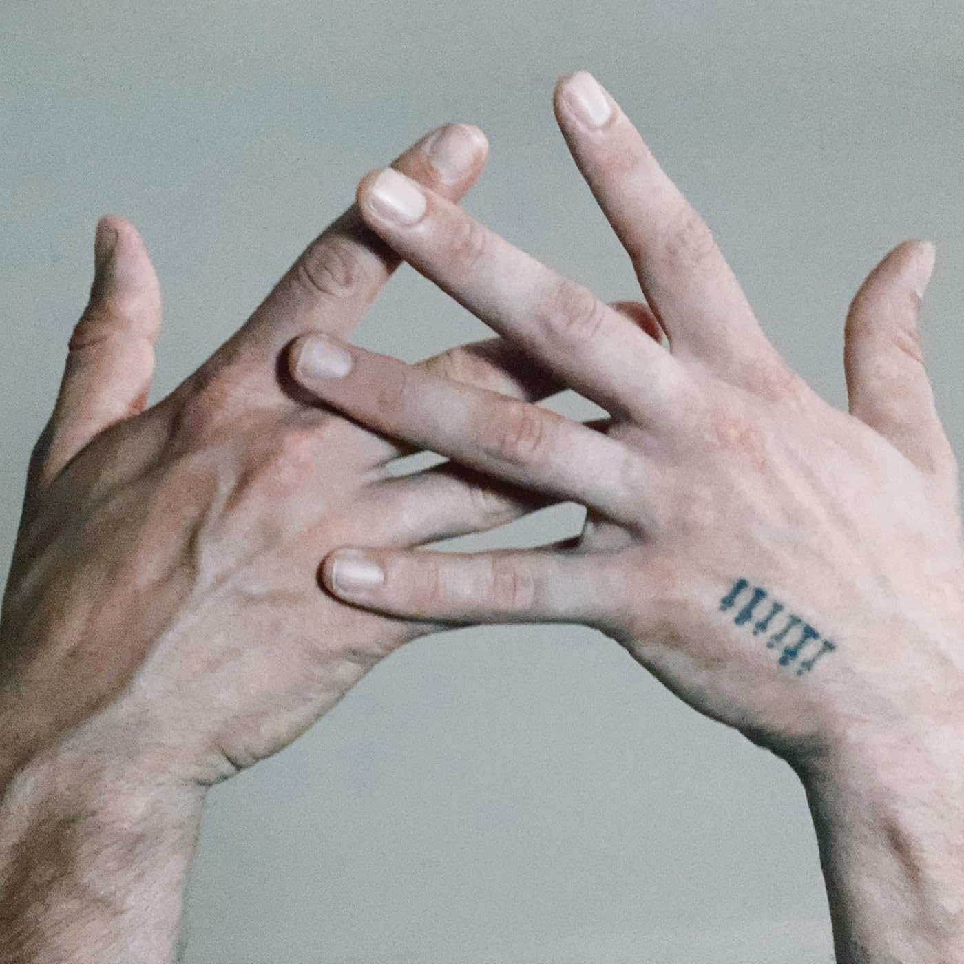 Two hands with intertwined fingers and a small tattoo.