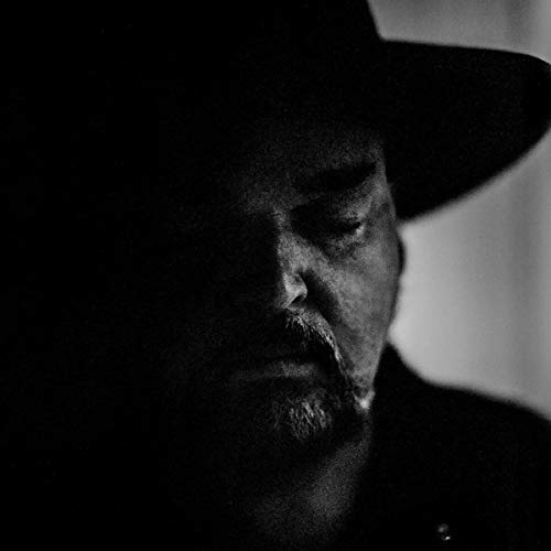 Black and white close-up portrait of a man wearing a hat, with a shadowed face.
