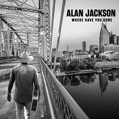 Alan Jackson in a cowboy hat walks across a bridge toward a city skyline.