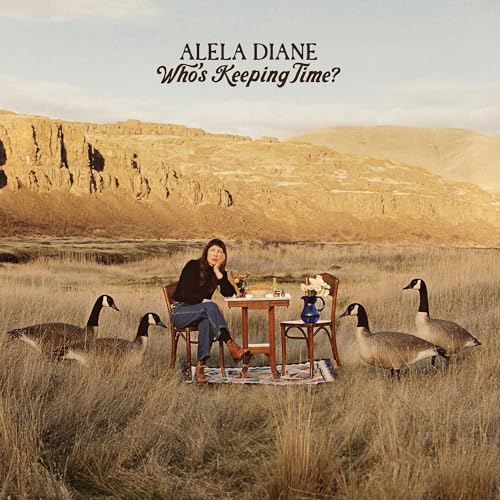 Woman seated at a table with geese in a grassy landscape.