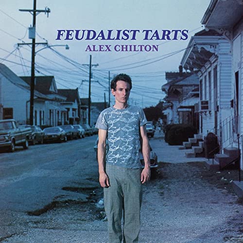 Alex Chilton stands on a street in a blue-toned photo with album text above.