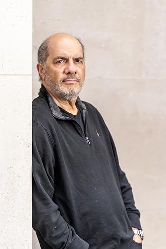 A middle-aged man with a beard wearing a black quarter-zip sweater leaning against a wall.