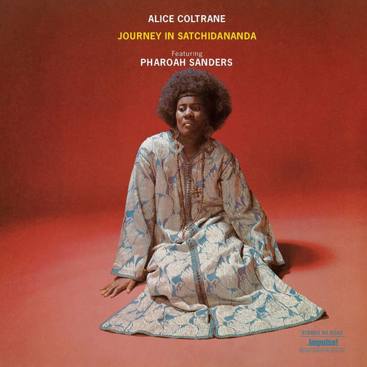Alice Coltrane sits on a red background wearing a patterned kaftan and large afro.
