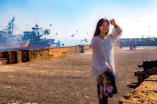 Woman smiling in front of a harbor with ships and cannons.
