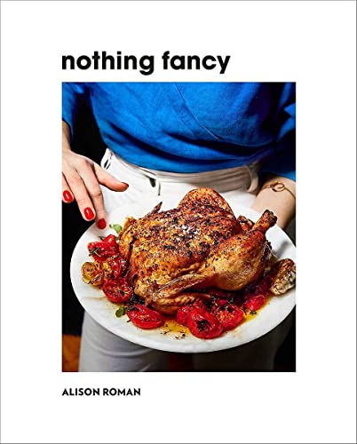 A person in a blue shirt holds a roasted chicken with tomatoes on a plate.