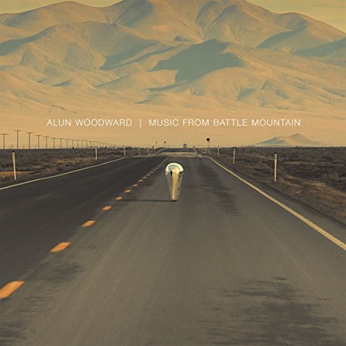 A metallic, teardrop-shaped object sits on a desert road leading toward distant mountains.