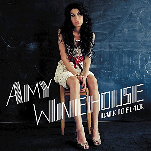 "Amy Winehouse sits on a stool, wearing a white dress, against a dark background."
